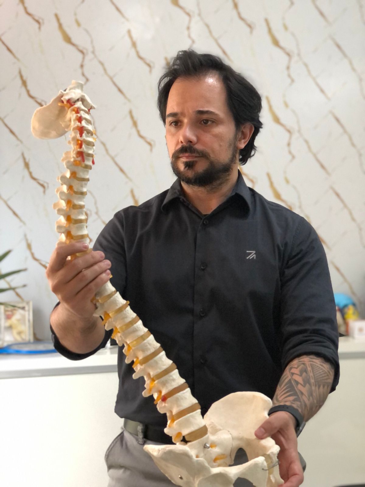 Dr. Kleber Santos segurando um modelo anatômico da coluna no consultório Osteogyn, clínica de osteopatia em Goiânia